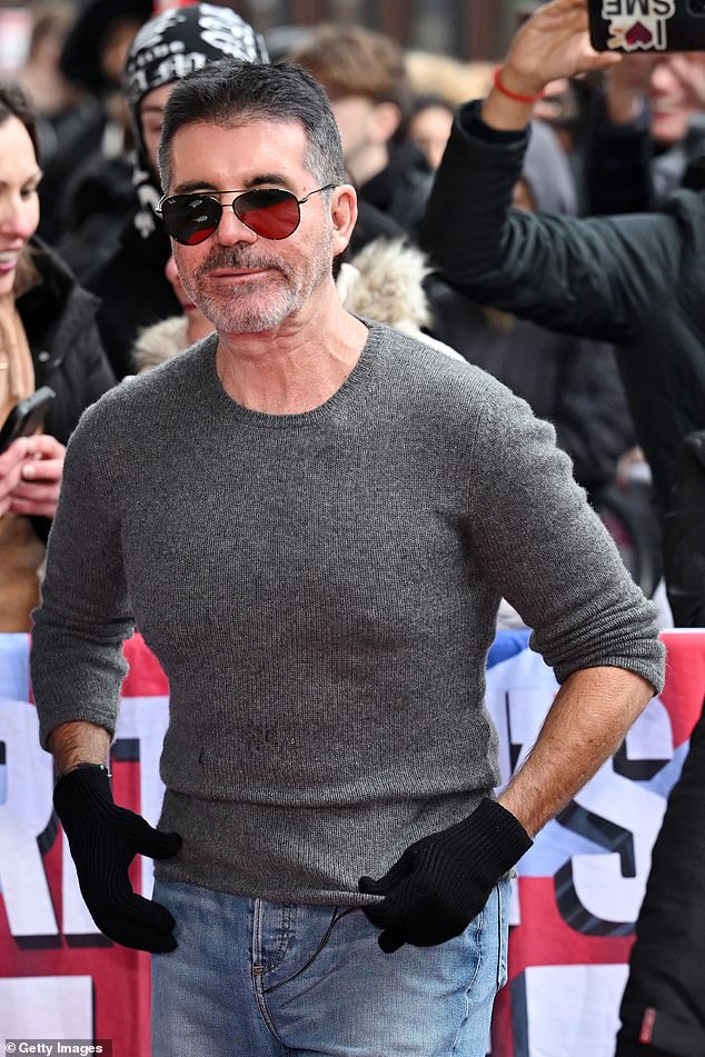 Simon Cowell, 64, made a bizarre display on the carpet as he took off his coat but opted to leave his black gloves on.