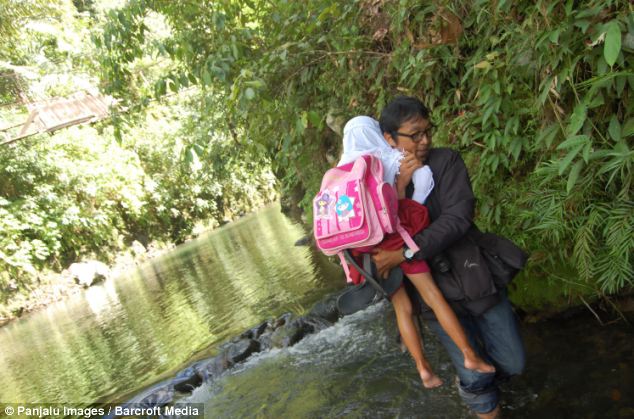 The school run: a man carries his daughter across water to take her to school because there is no road access to the town