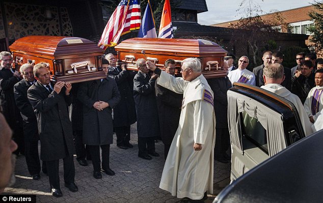 Blessing: A priest sprinkles holy water on the coffins after the funeral