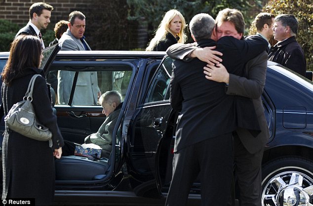 Solemn: Mourners embrace while a family member waits in a limousine to drive to the cemetery after the funeral.
