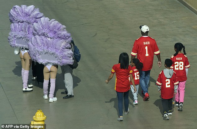 A family of Chiefs fans walks alongside a pair of Showgirls before Super Bowl LVIII in Las Vegas.