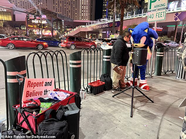 A street preacher is seen offering a prayer for a man dressed as Sonic The Hedgehog