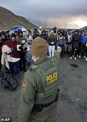 A Border Patrol agent asks asylum-seeking migrants to line up at a makeshift mountain camp