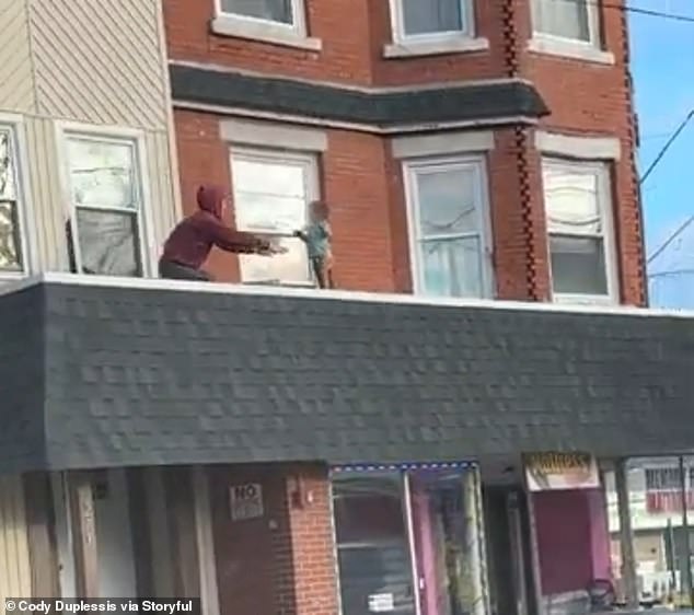 The man is seen extending his hands towards the baby just before picking him up and bringing him back through the open window.