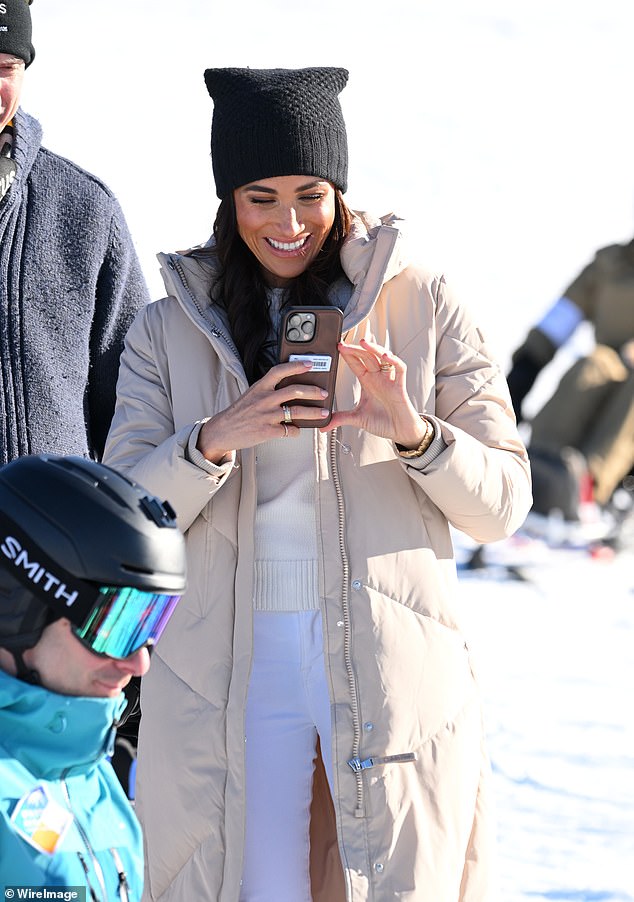 Meghan laughs as she appears to be collecting content on her phone while enjoying the tracks yesterday.