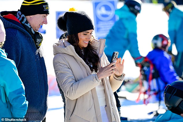 Meghan appeared to be filming or taking photographs yesterday, watched by an Invictus official on the slopes.