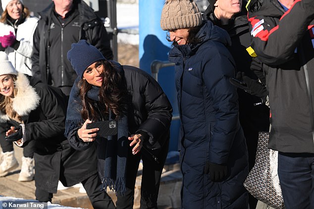 Proud Meghan watched and took videos and photos of Harry as he reached the end of the toboggan run.