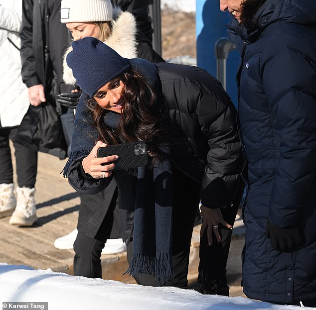 The mother-of-two bundled up in a black puffer jacket, black jeans and a navy blue beanie and scarf, while also sneaking a peek at her large engagement ring.