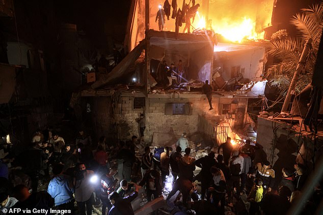 People watch as others search for victims in the rubble of a burning building, following an Israeli attack in Rafah, in the southern Gaza Strip.