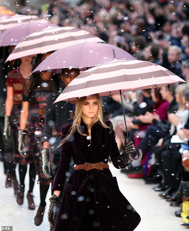 Cara Delevingne holds an umbrella while walking the Burberry runway in 2012