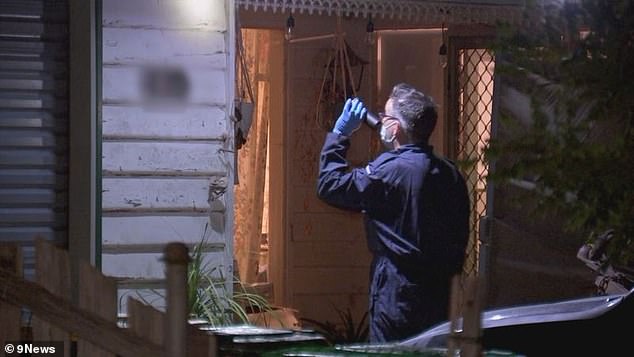 A forensic police officer examines the house on Friday night. It is understood the woman's two teenage children were at the property and are being cared for by neighbours.