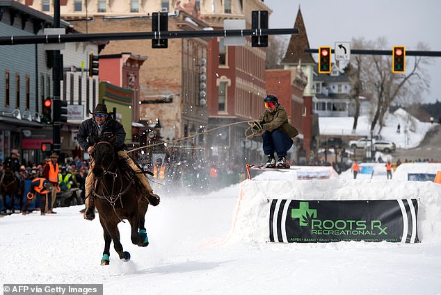Cyclist Carl Gomez races down Harrison Avenue as skier Ben Southworth performs a jump during the 75th annual Leadville SkiJoring weekend competition in Colorado on March 4, 2023.