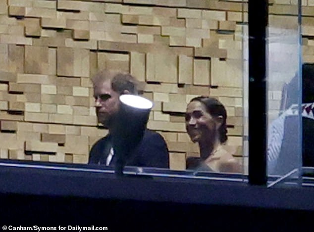 Prince Harry appeared pensive walking down a hallway at the event on Friday night. Megan smiled.
