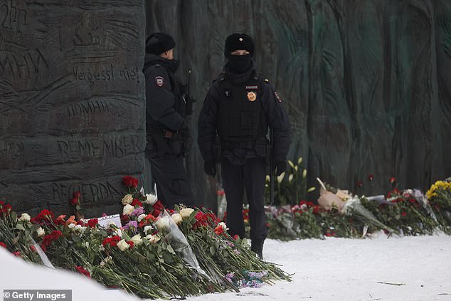 Russian police officers next to flowers near the Wall of Sorrow monument placed in memory of Alexei Navalny