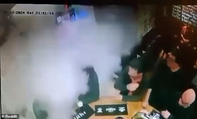 A sudden explosion of foam erupts from the fire extinguisher, which spins on the ground, causing the dog to cower in shock and the punters to be showered in foam.