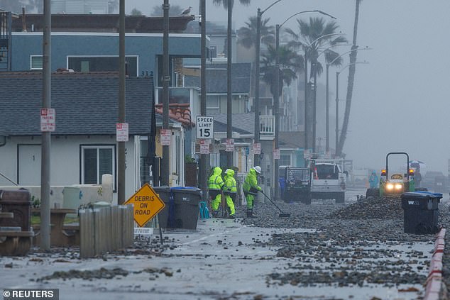 Work crews clear a beachfront road after ocean waves caused by a winter storm pushed rocks off the beach in Oceanside, California, on Tuesday.