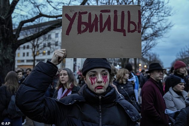 A woman holds a sign with her face painted the color of blood during a protest in front of the Russian embassy in Berlin, Germany, Friday, February 16, 2024.