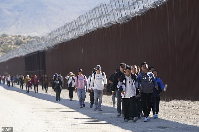 A group of people, including many from China, walk along the wall after crossing the border with Mexico to seek asylum on October 24 near Jacumba, California.