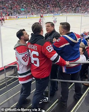 The Devils fan, wearing a replica of Jack Hughes' No. 86 jersey, is seen arguing with another man in a winter jacket along a staircase in one of the lower sections of the Prudential Center.