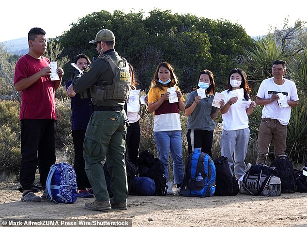A migrant from China holds his passport and documents as he is photographed by a U.S. Border Patrol agent in an outdoor waiting area as they prepare to board a bus to a processing facility near the small community. desert border of San Diego County.  Jacumba Hot Springs in December 2023