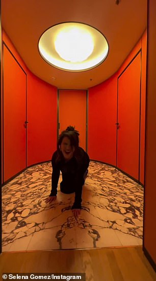 She was wearing a long-sleeved black turtleneck dress and had her hair styled in a messy bun as she walked through a bright orange room with marble floors.