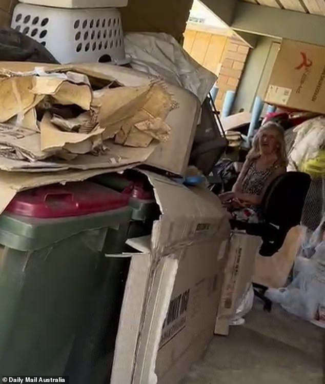 Maree sits among trash strewn across her garage hours after her brother was found rotting inside.
