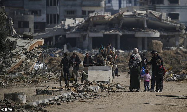 Palestinians walk past destroyed houses in Al Nusairat refugee camp