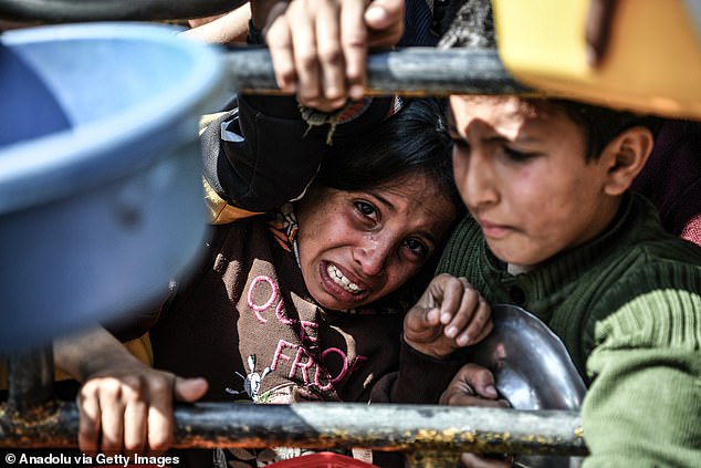 A boy is trapped as Palestinians spread out their empty containers to be filled with food, distributed by charities, behind bars as they are unable to obtain basic food supplies due to the embargo imposed by Israeli forces in Rafah, Gaza, on Sunday .