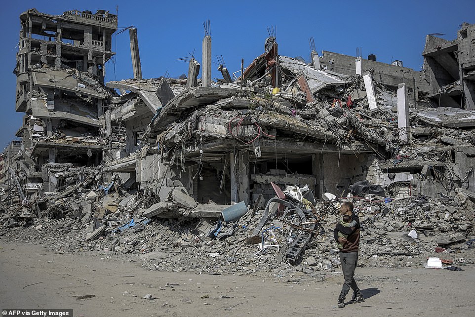 A Palestinian carries a baby in front of buildings destroyed during Israeli attacks in Beit Lahia, northern Gaza.