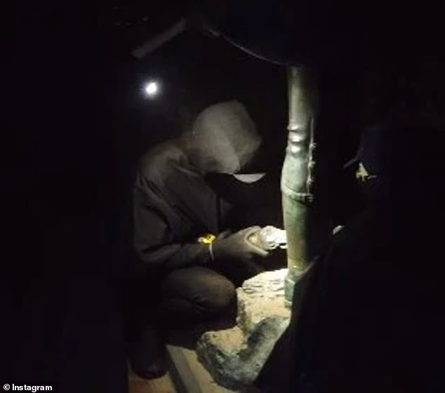 Images posted online appear to show a masked individual dressed all in black using an angle grinder to cut the statue from its pedestal before it fell to the ground (pictured)