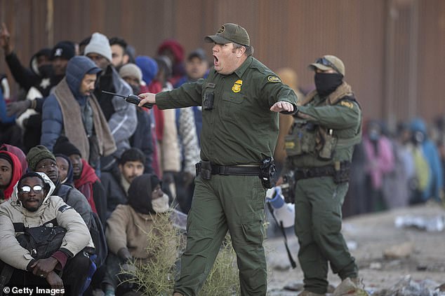 A U.S. Border Patrol agent yells at migrants who had gotten into a long line of people waiting to be transported from the U.S.-Mexico border on Dec. 6, 2023.
