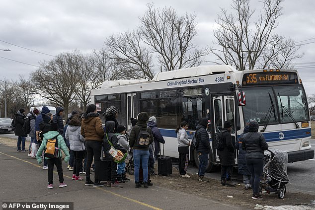 Newly arrived migrants wait at a bus stop in front of the Floyd Bennet Field shelter on February 21, 2024 in the Brooklyn borough of New York.