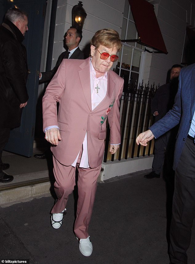 Wearing a pink suit and his trademark red-tinted glasses, the singer also sported a foot brace as he was helped down the stairs of Robin Birley's private members club in Mayfair.