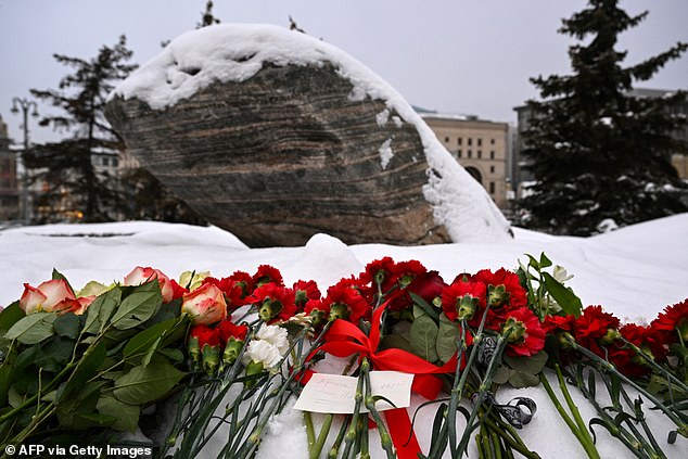 a paper note reading "Hello.  This is Navalny" He is seen among flowers left for the late Russian opposition leader Alexei Navalny at the Solovetsky Stone, a monument to political repression that has become one of the sites of tribute to Navalny, in Moscow on February 23.