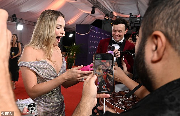 Margot Robbie reacts after receiving a packet of Tim-Tams on the red carpet at the 2024 Australian Academy of Film and Television Arts (AACTA) Awards