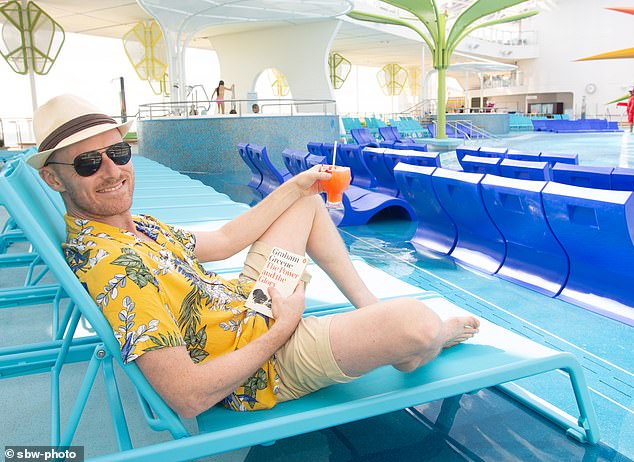 Thomas W. Hodgkinson enjoys a drink with his book while lounging by the pool on board