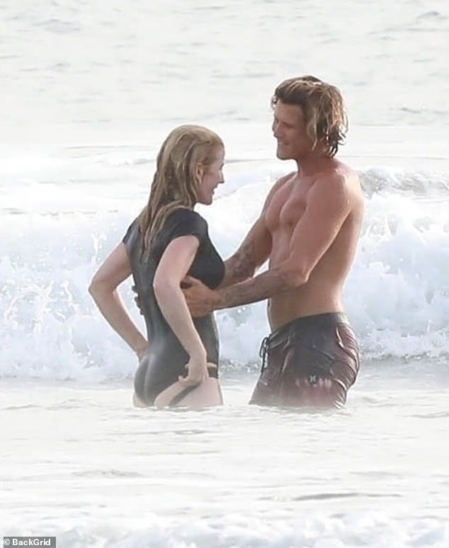 Handsome surf instructor Armando Pérez holds a smiling Ellie close as the waves roll in