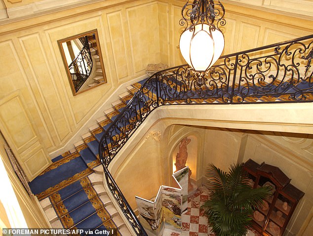A wide staircase is lined with a royal blue and gold rug.