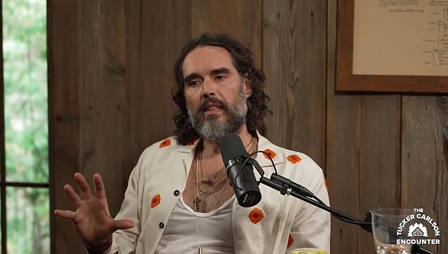 Russell Brand, pictured speaking at The Tucker Carlson Encounter, has been accused of sexually assaulting a woman on a film set in 2010.