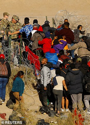 Migrants seeking asylum in the United States try to cross a barbed wire fence on the southern border