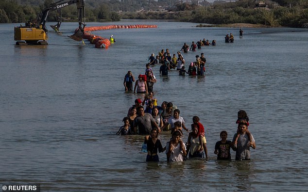 A caravan passes by a series of buoys, which are being built to deter migrants crossing the Rio Grande, as they search for an opening in the concertina wire to enter Eagle Pass, Texas, USA, July 27, 2023.