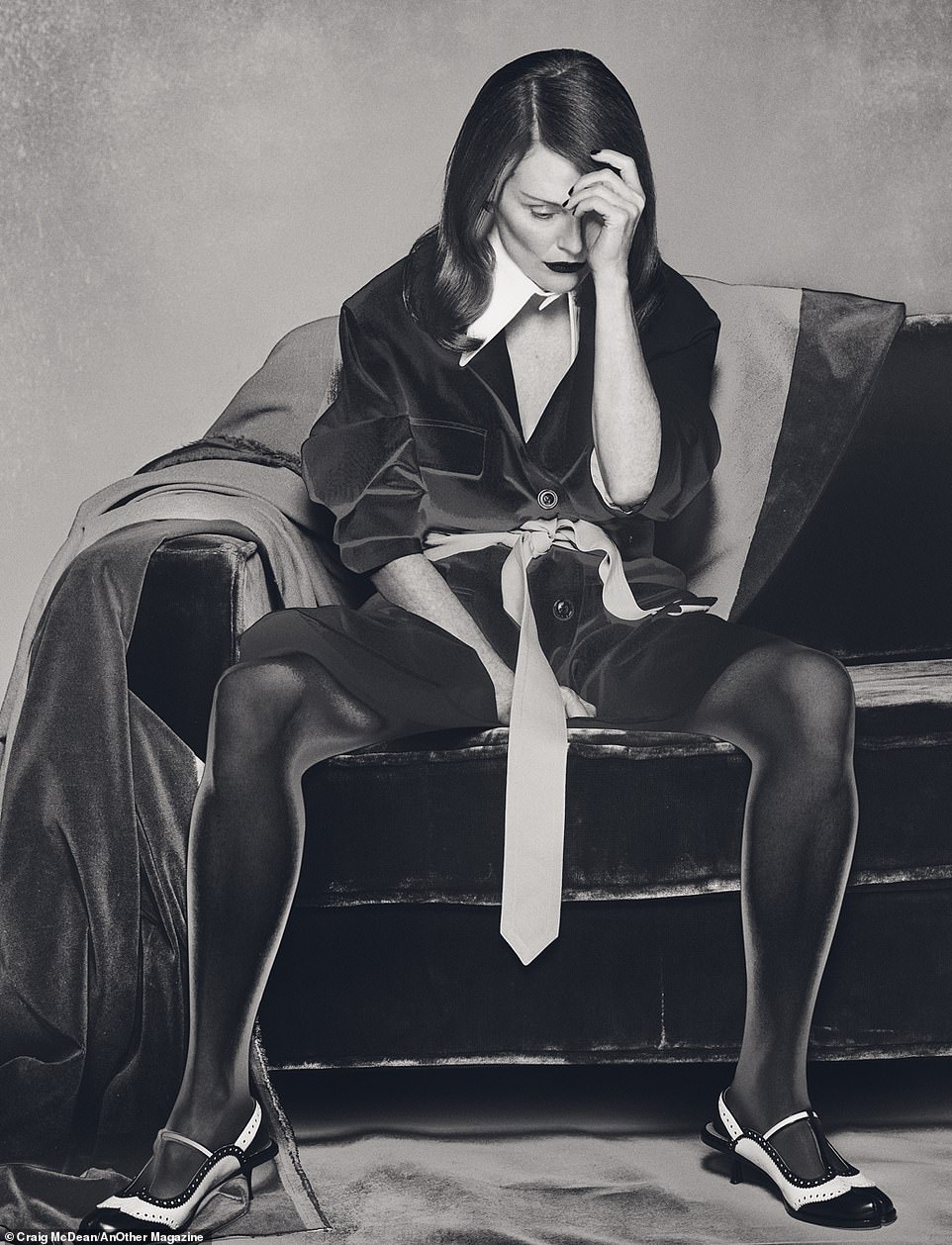 Another photo taken by photographer Craig McDean and styled by Katie Shillingford shows Julianne sitting on a couch looking dejectedly at her hand while wearing a velvet jacket with a large, pointed white collar and a men's tie as a belt from Maison Margiela.