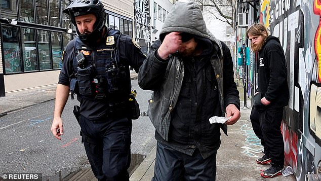 The measure makes possession of small amounts of drugs such as heroin or methamphetamine a misdemeanor, punishable by up to six months in jail (pictured: Police officer David Baer removes a man who was caught smoking fentanyl)