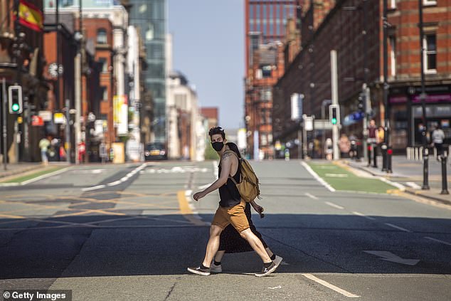 A man wearing a face mask crosses the street as he walks through central Manchester in April 2020.