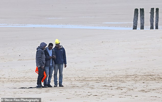 A group of migrants seen today walking back along a beach in Calais after a failed attempt to cross