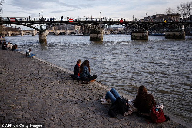 People sit on the bank of the Seine River to enjoy the warm weather in front of the Pont des Arts in Paris on February 15, 2024.