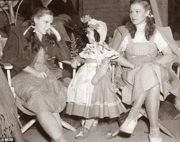 Pictured: Judy Garland sits with her stand-in Caren Marsh Doll and a munchkin on the set of The Wizard of Oz.