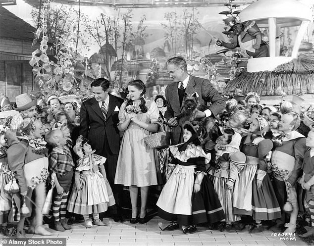 Pictured: Judy Garland on the set of The Wizard of Oz with producer Mervyn LeRoy and director Victor Fleming, along with ToTo and the munchkins.