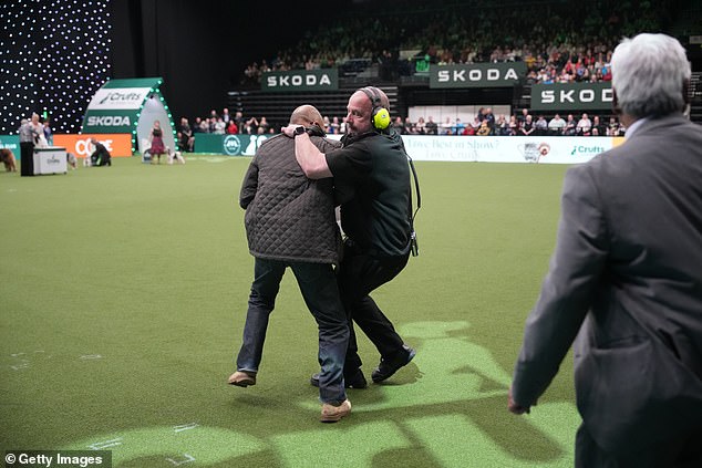 A protester is challenged by security during Crufts 2024 at the NEC Arena
