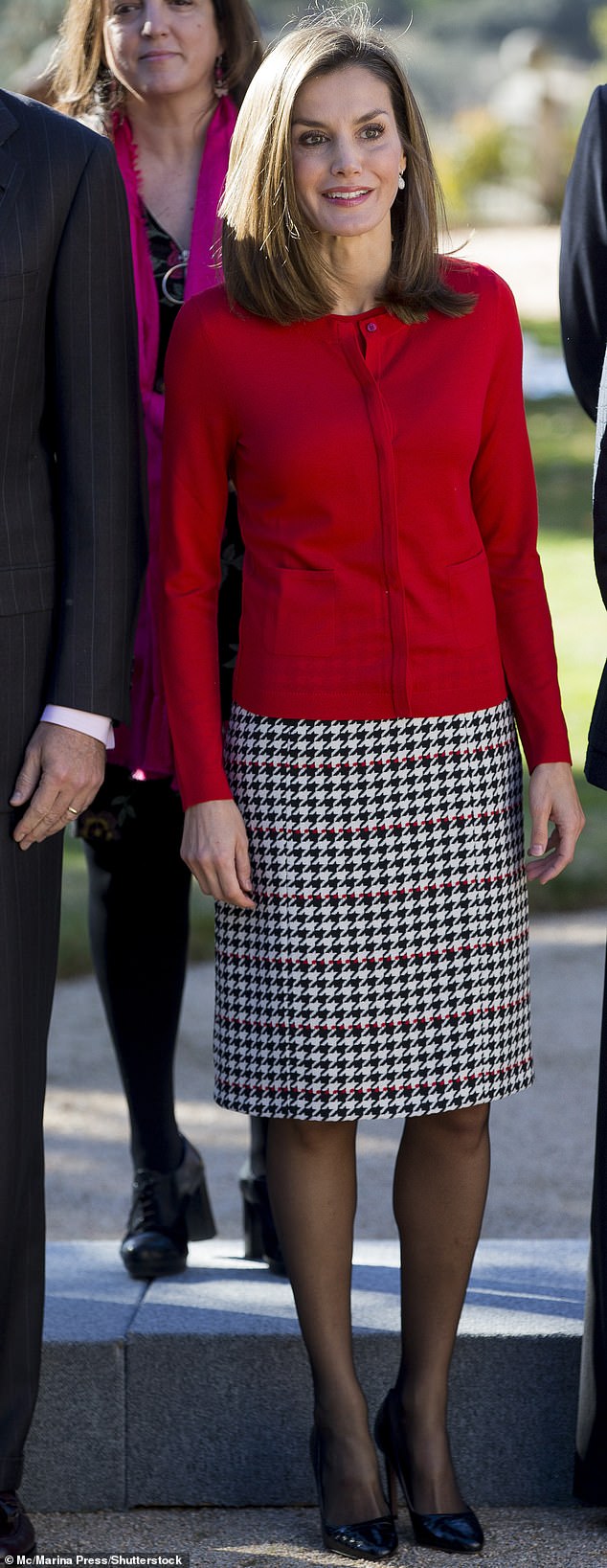 Queen Letizia of Spain draws attention to the red accents of her houndstooth tweed skirt by wearing a red cardigan on the top half.